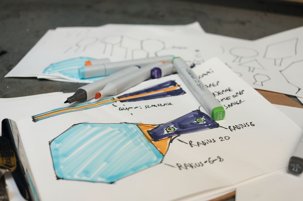 Designskisse av rekkert sett ovenfra og i profil. De ulike elementene er fargelagt med ulike farger, og detaljer som radius og gummislagflate er skrevet inn på skissa. Foto.