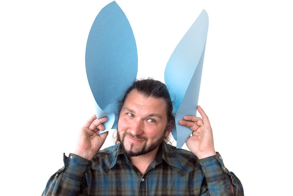 En mann holder store foldede papirører foran ørene sine. Foto.