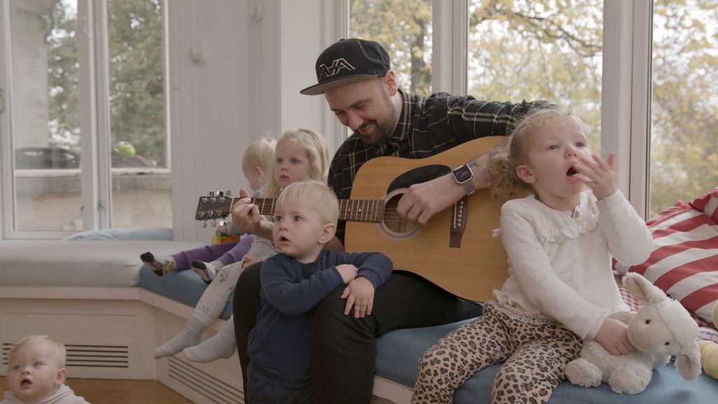 En mannlig barnehageansatt med gitar og flere små barn rundt seg. Foto.