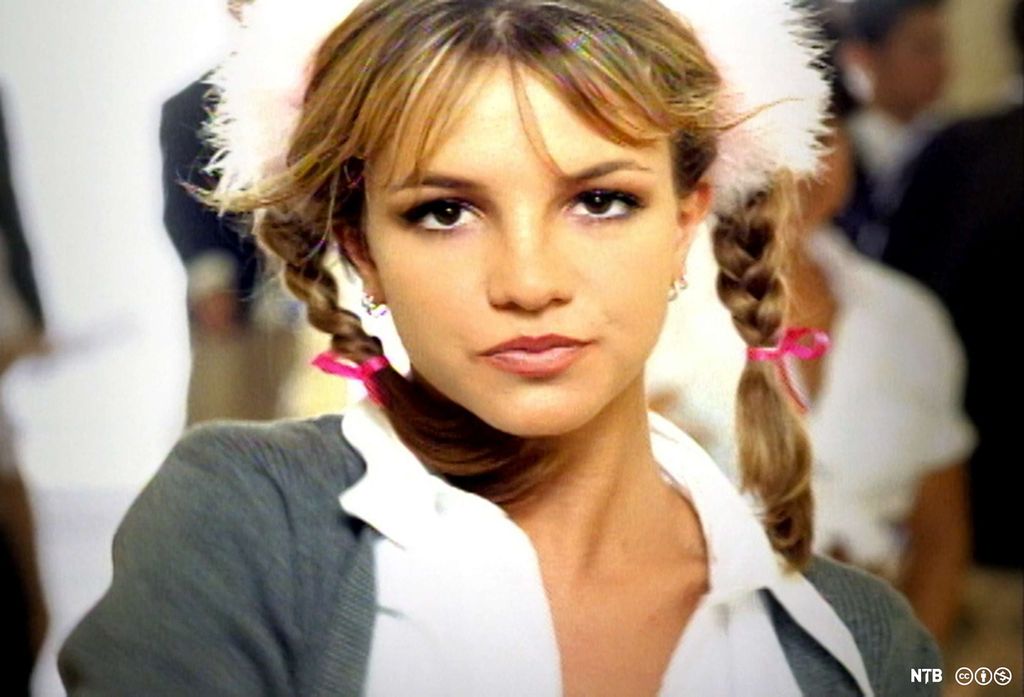 Ei ung Britney Spears ser alvorleg inn i kameraet. Ho har musefletter og grå skuleuniform. Stillbilete frå musikkvideoen "Baby One More Time".