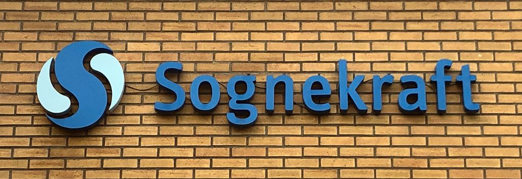 Logo og navnet Sognekraft med blå, frittstående bokstaver på en gul murvegg. Foto.
