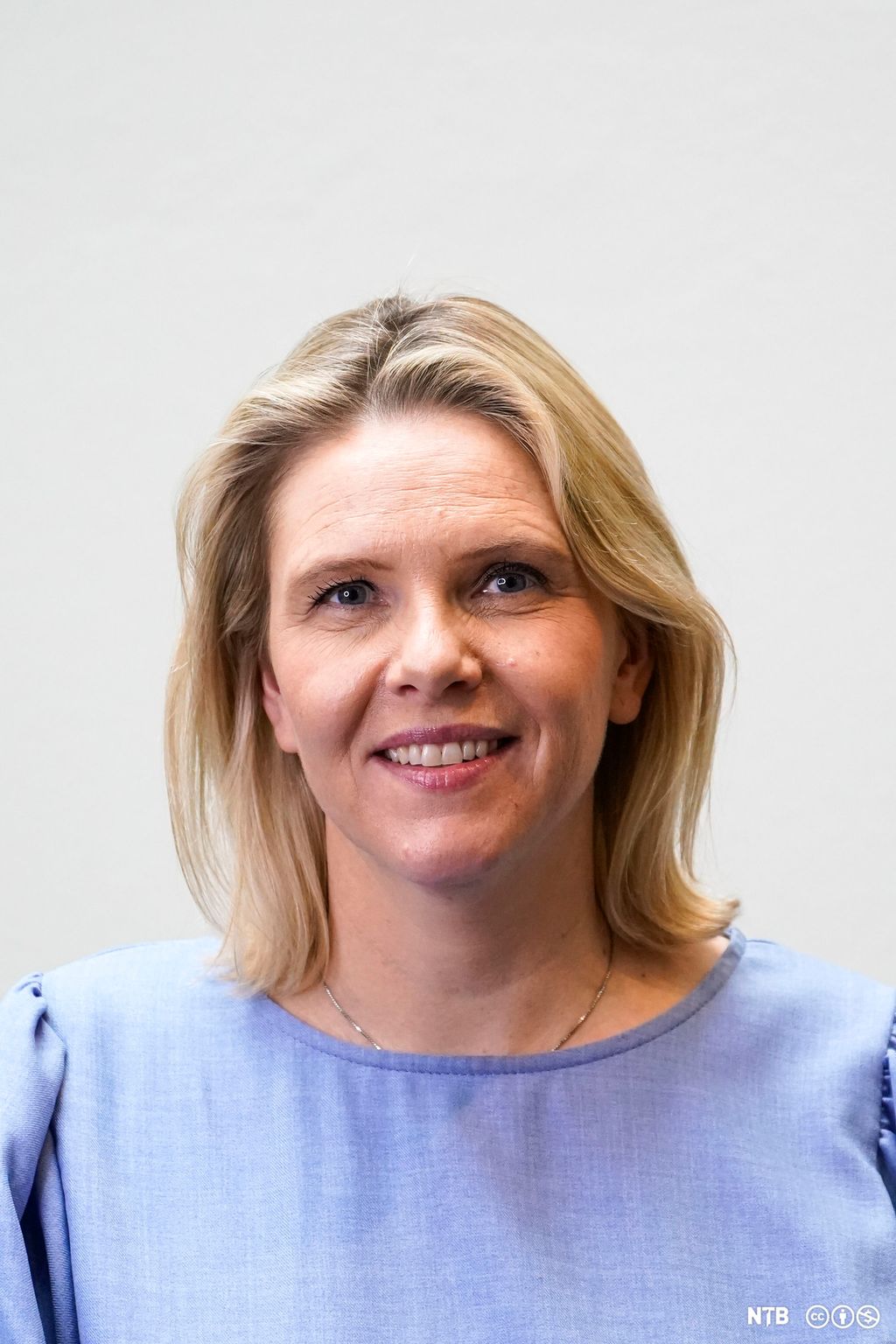 Portrett av Sylvi Listhaug. Hun har lyseblå bluse og blondt hår. Hun smiler og ser rett inn i kamera. Foto.