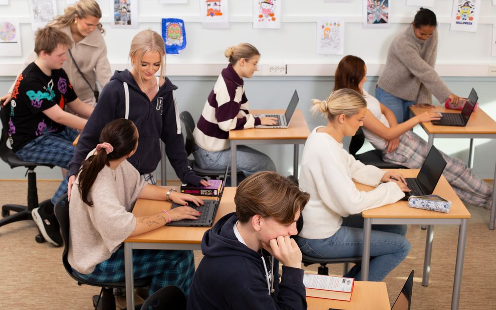 Flere elever i et klasserom. Noen skriver, og noen snakker sammen. Foto.