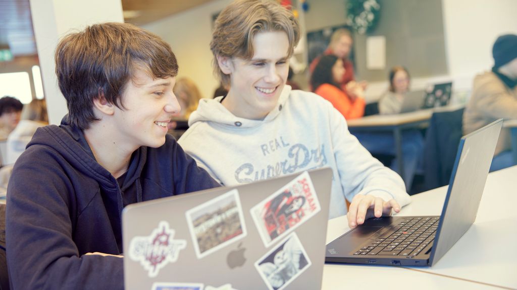 To unge gutter jobber sammen foran laptopene sine. Foto.