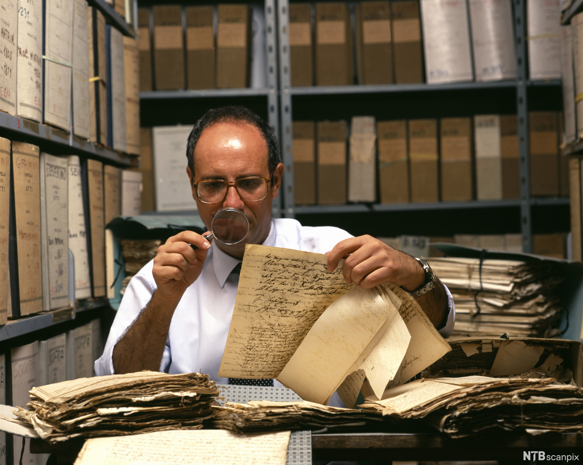 Mann studerer gamle papirer med forstørrelsesglass. Foto.