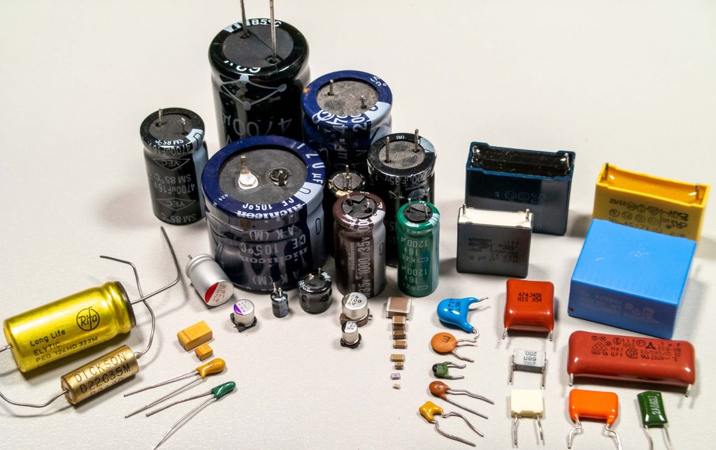 Ei samling kondensatorer. De fleste har en sylindrisk kropp og to tilkoplingsbein på den ene sida. Noen få er tilnærma rektangulære, med to tilkoplingsbein på den ene sida. Foto.