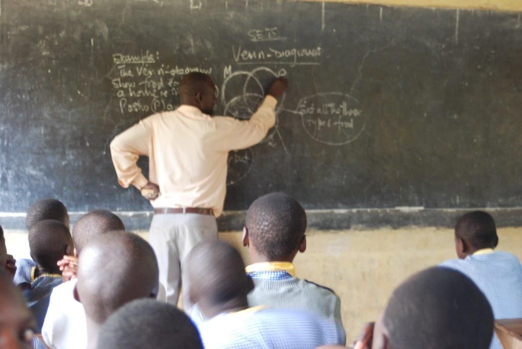 Lærer skriver og tegner venndiagram på tavla. Elever sitter ved pultene sine og ser på. Alle har ryggen til kameraet. Foto.