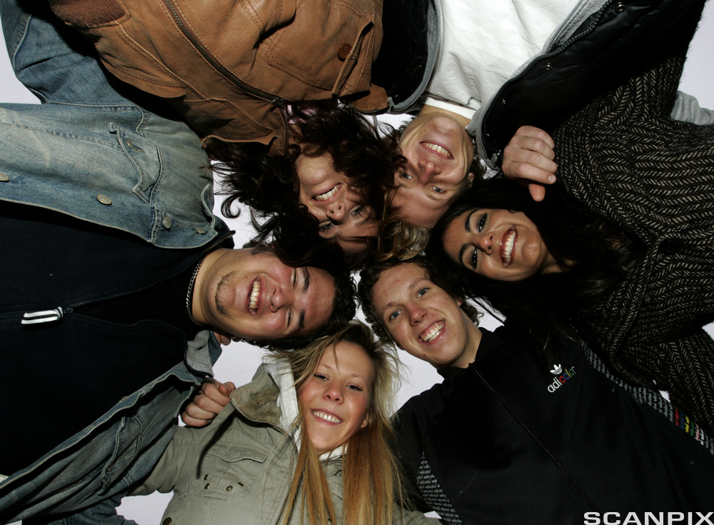 Seks glade elever i skolegården. De står  med hodene tett inntil hverandre og holder rundt hverandre. Vi ser ansiktene deres i froskeperspektiv – nedenfra og opp. Foto.