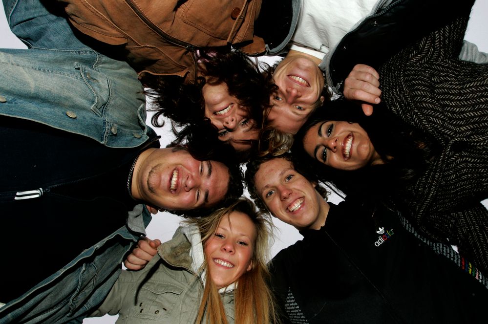 Seks glade elever i skolegården. De står med hodene tett inntil hverandre og holder rundt hverandre. Vi ser ansiktene deres i froskeperspektiv – nedenfra og opp. Foto.