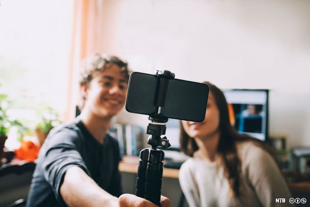 To personer filmer seg selv med en mobiltelefon som de holder på stativ. Foto.