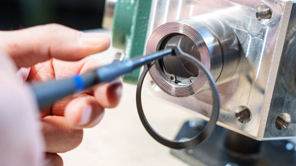 Ei hånd holder ei tang som klemmer mot en ring. Foto.