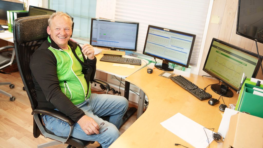 Smilende mann på kontor foran flere dataskjermer. Foto.