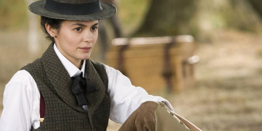 Kvinne med hvit bluse, vest, oppsatt hår og hatt. Foto.