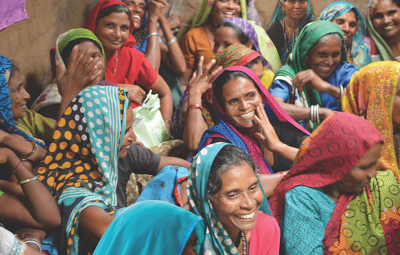 Women in colourful shawls sitting close together. They are smiling. Photo.