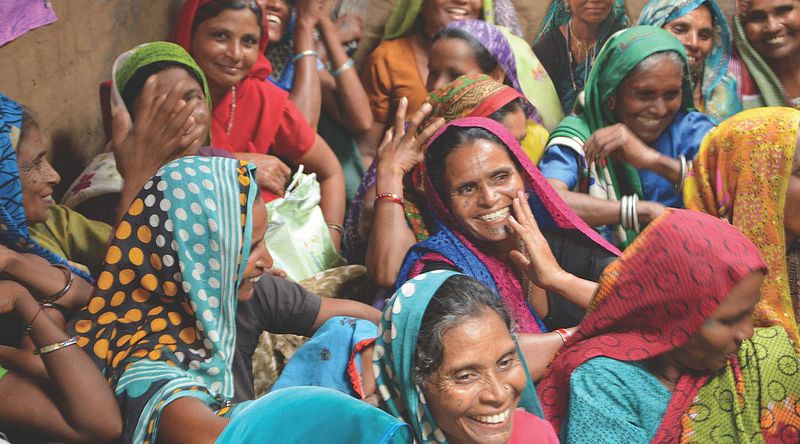 Women in colourful shawls sitting close together. They are smiling. Photo.