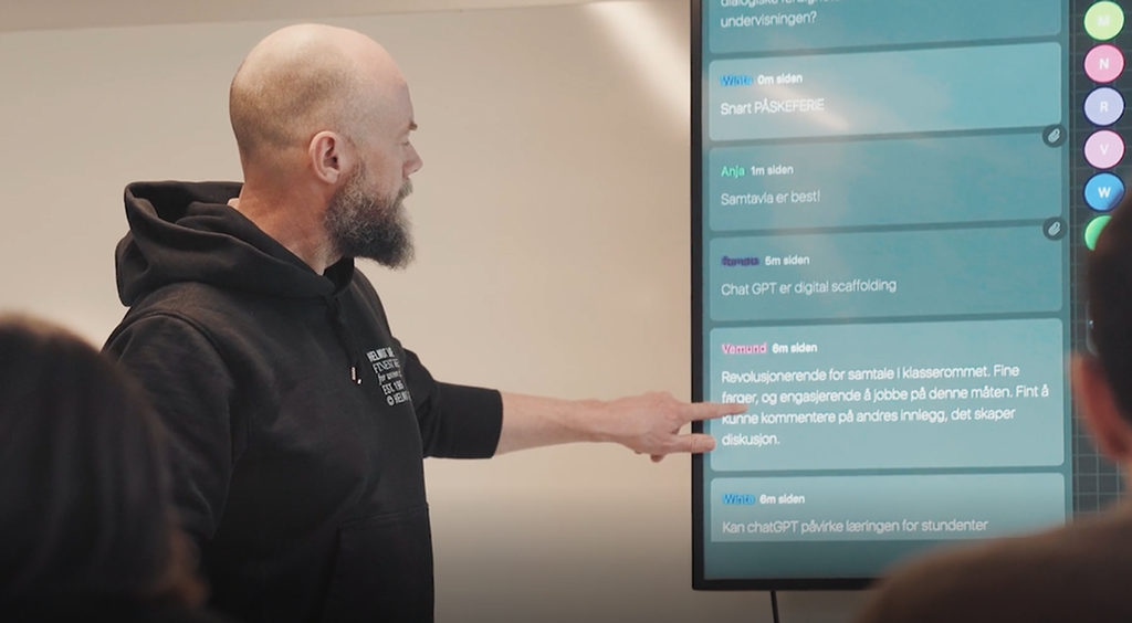 Mann står og peker på ei smal digital tavle med innlegg fra flere ulike personer. Foto.