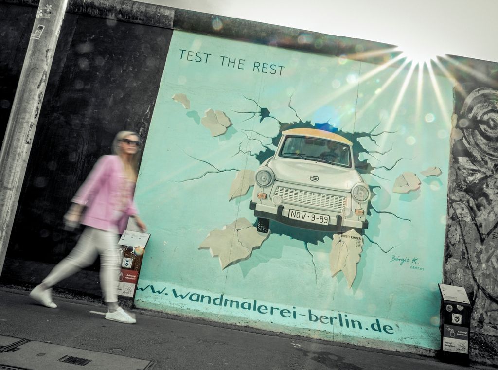 Gatekunst som viser ein Trabant-bil som har køyrt gjennom og knust Berlinmuren. Foto.