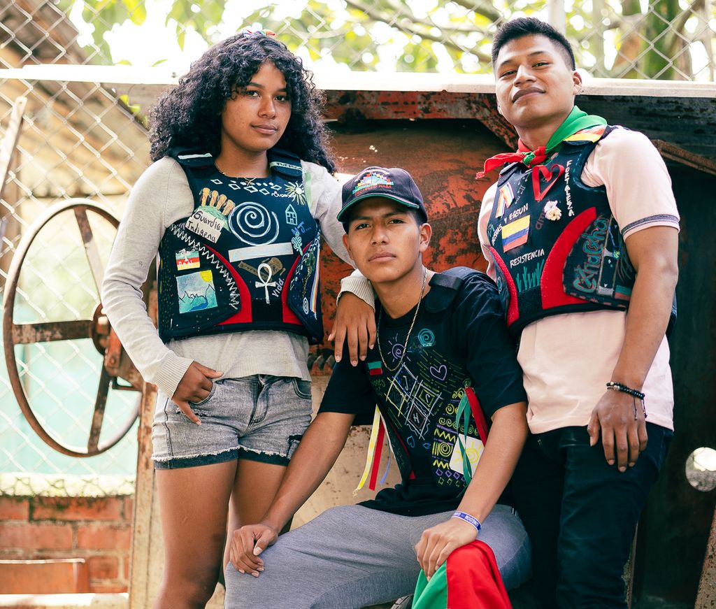 Tre unge personer har på seg skuddsikre vester som er dekorerte med ulike symboler og tegninger. Foto.