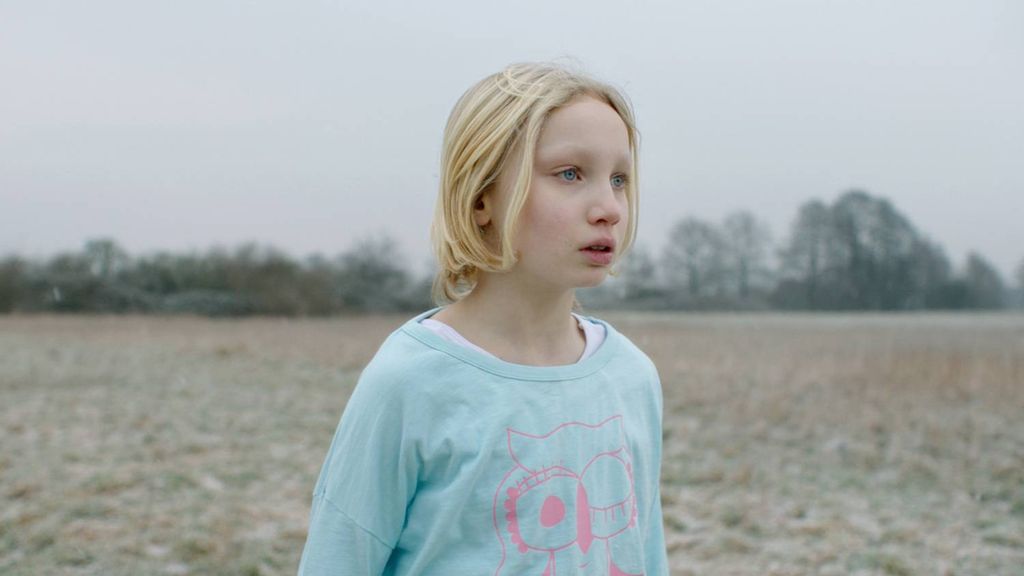 Ei ung jente i lys tyrkis overdel står aleine ute på ei slette. Stillbilde frå filmen "Systemsprengeren".