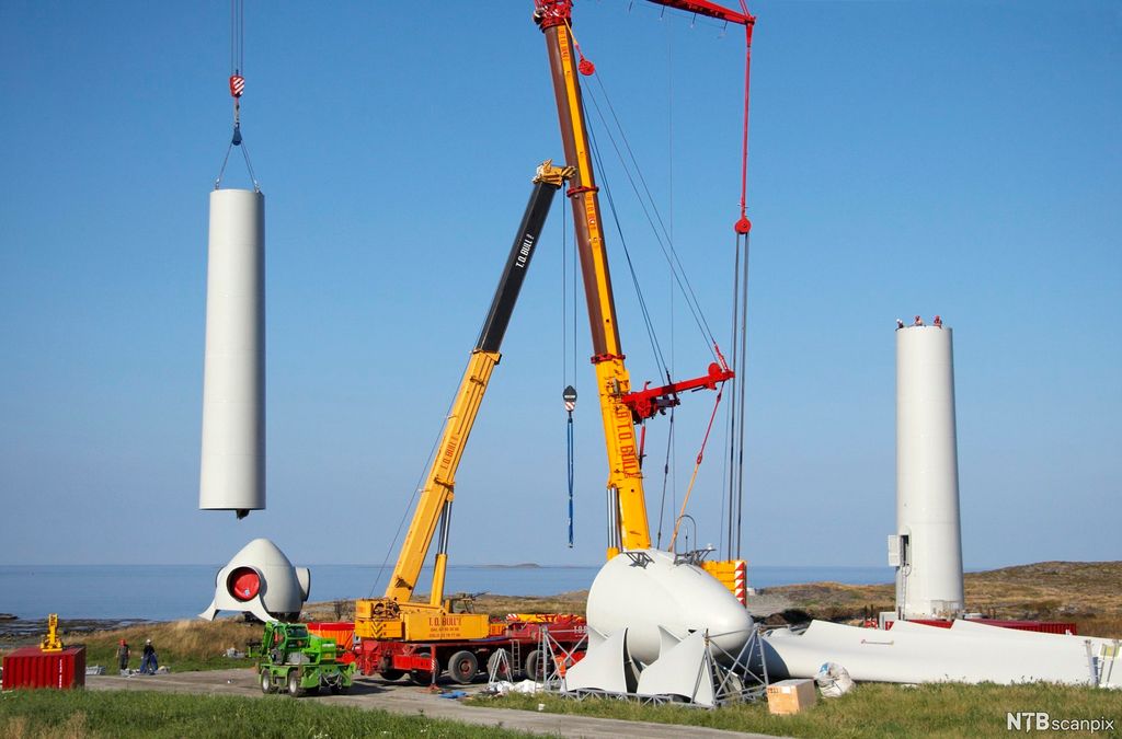 Mobilkran heiser på plass deler av vindturbin i naturområde. Foto.