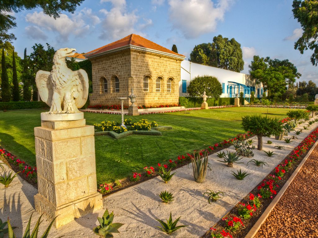 Murhus med hage rundt. Statue av ørn i forgrunnen. Foto.