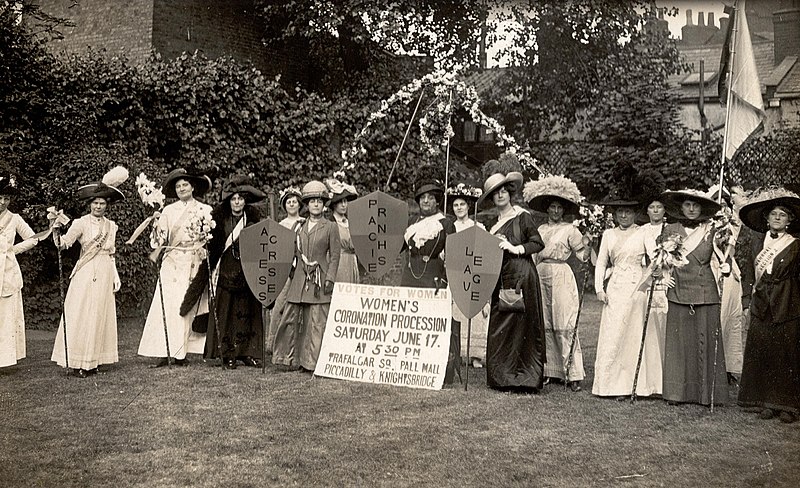 A photo taken at the end of the nineteenth century showing 16 middle/upper-class women dresses in the traditional dresses of the time. They are demonstrating for women's right to vote. 