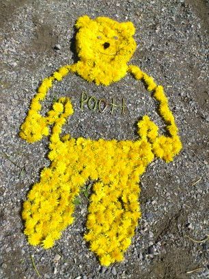 Ole Brumm laget av løvetannblomster på bakken. Foto. 