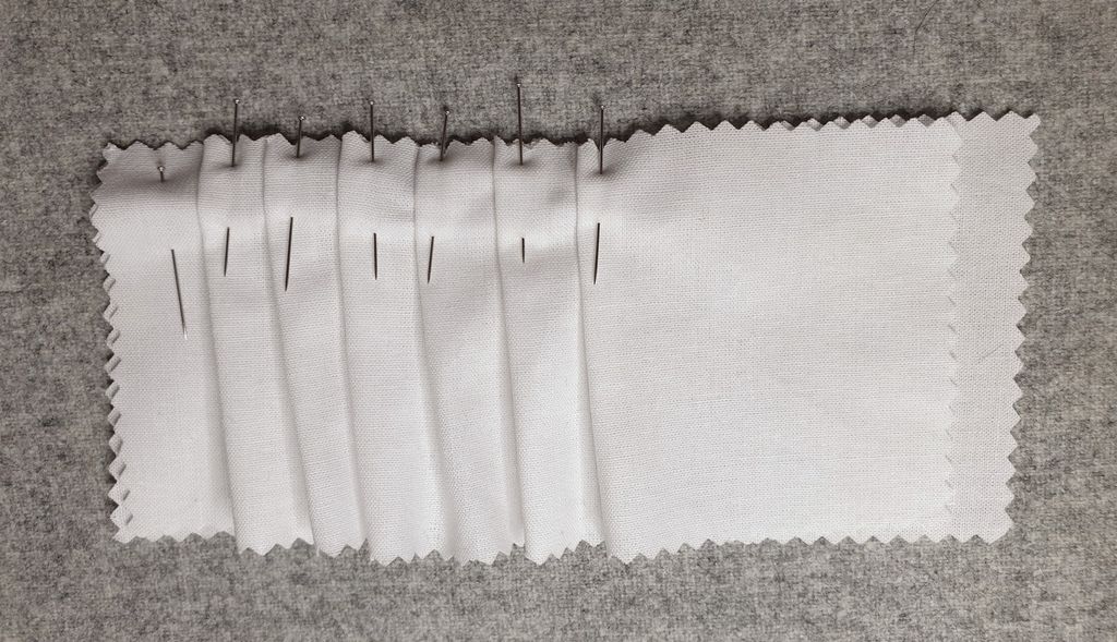 Fotografi av ein prøvelapp med faldar som er festa med knappenåler.