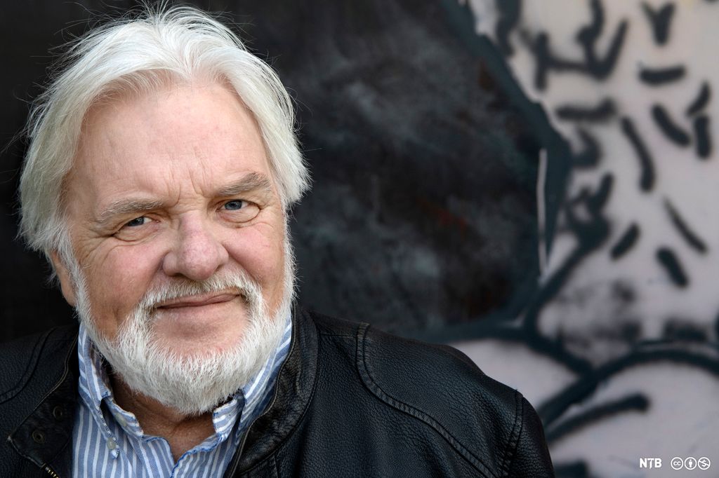 Portrettfoto av en smilende mann med skinnjakke og grått hår og skjegg.