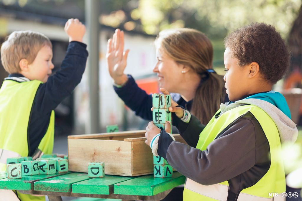En voksen gir high five til en gutt mens en annen gutt stabler bokstavklosser. Foto.