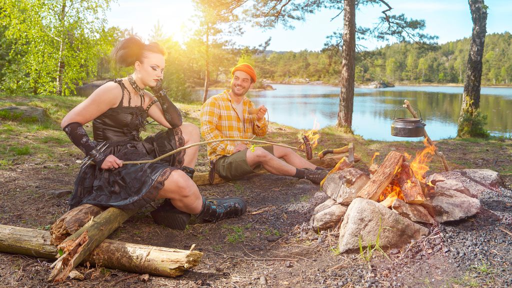 Gutt i turtøy og jente i gotisk tøy griller pølser i skogen. Foto.