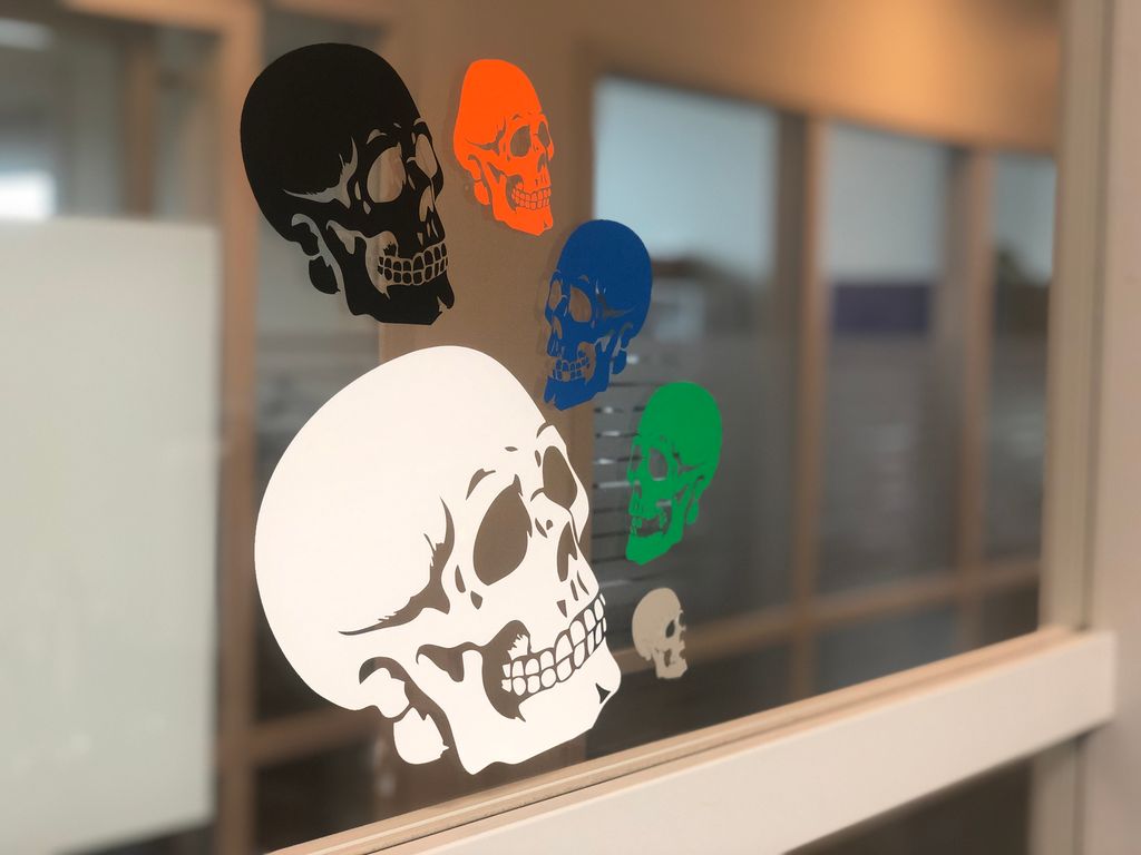 Stiliserte hodeskaller i ulike farger utført i vinyl hengt opp på et vindu. Foto