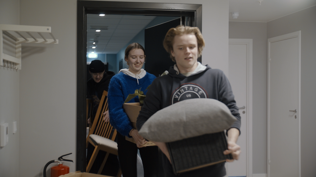 Ungdommar ber møbel inn i ei leilegheit. Foto.