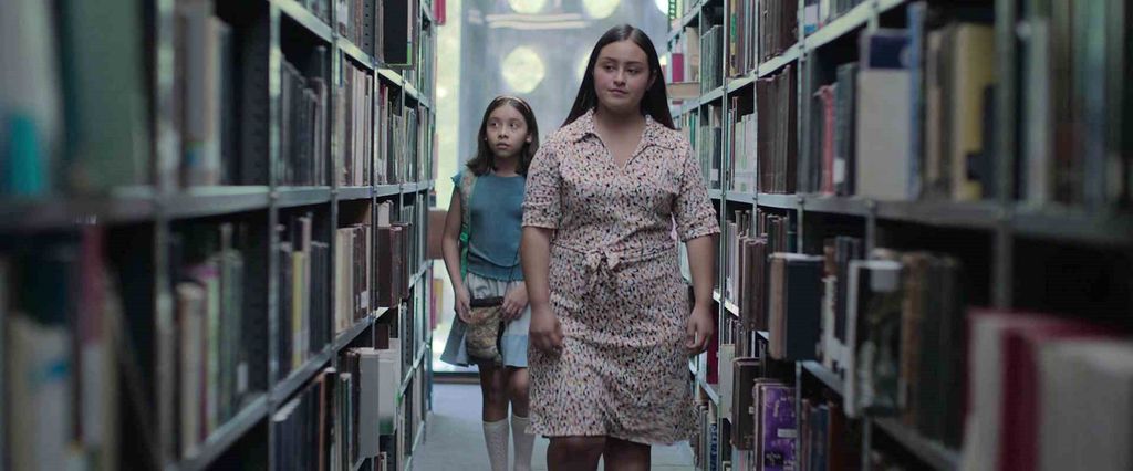 Ei ung kvinne og ei jente går mellom bokreoler på et bibliotek. Skjermutklipp fra filmen Radical.