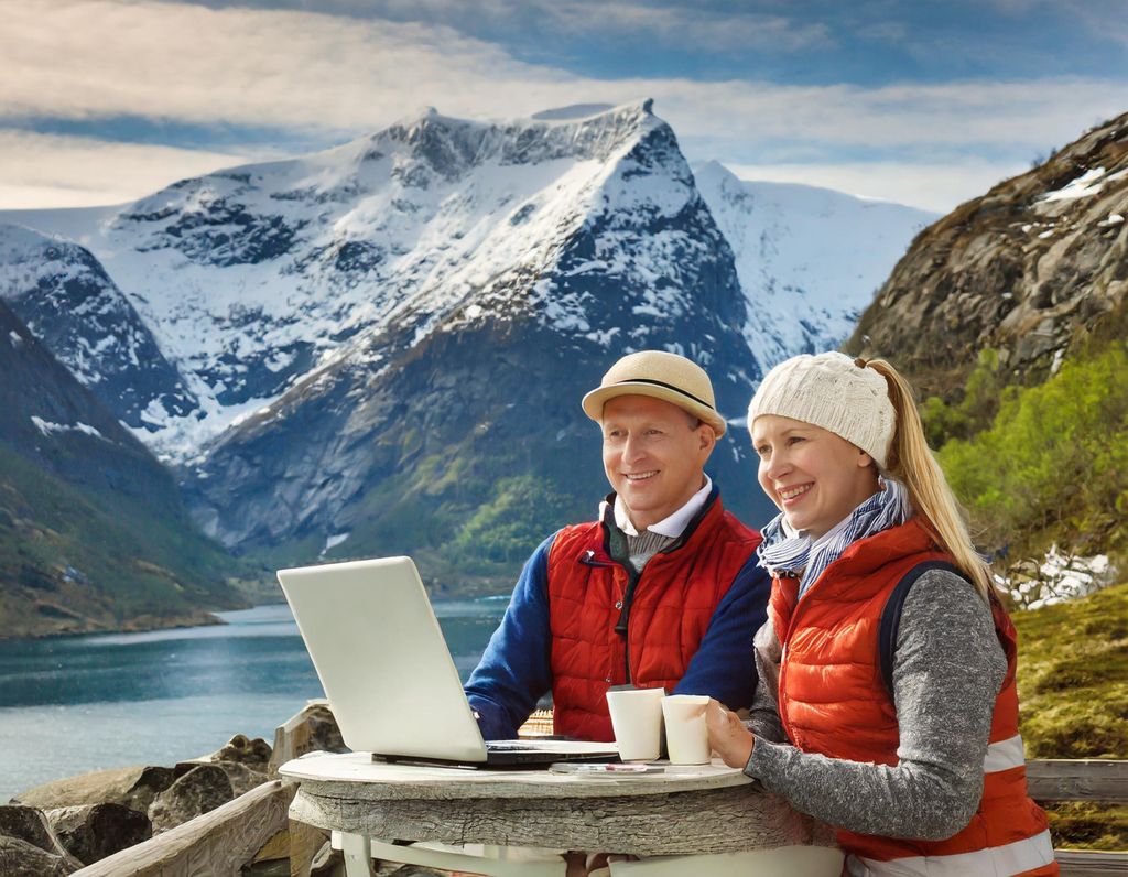 To personer med uteklær sitter ved datamaskin utendørs. KI-generert foto.