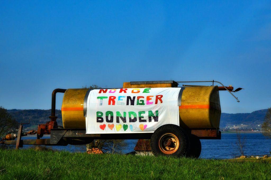 Plakat på gjødselspreiar på eit jorde. På plakaten står det: “Norge trenger bonden“. Foto.
