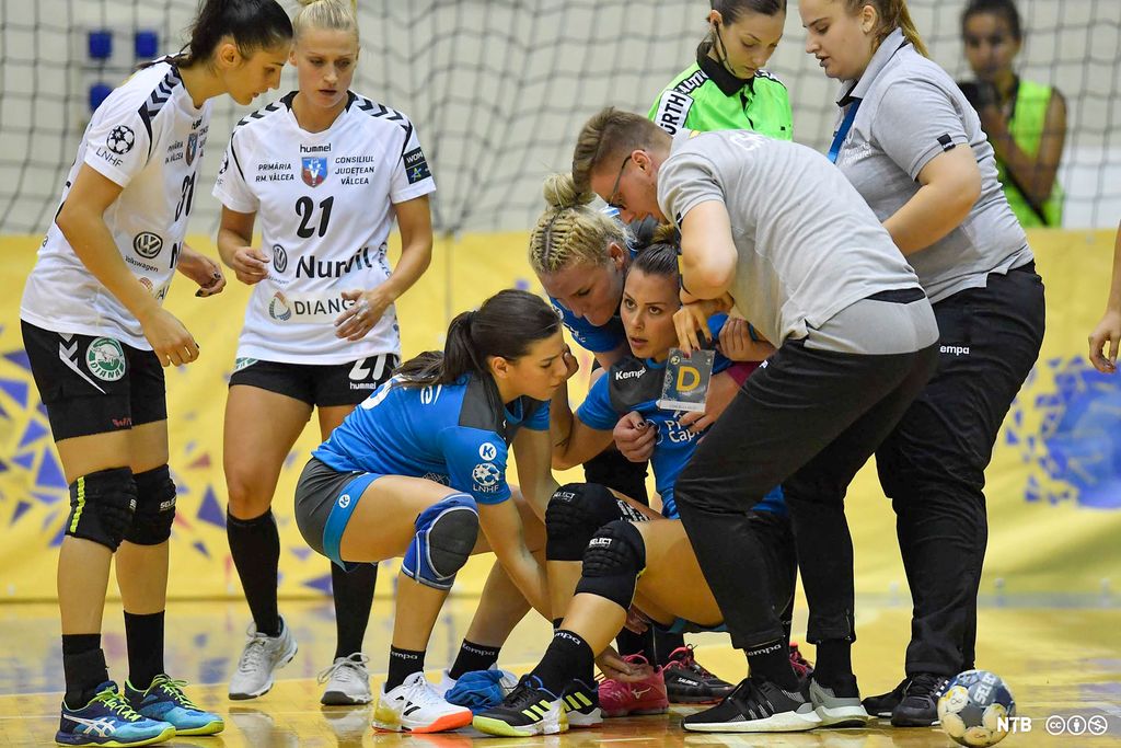 Lagveninner og personar frå støtteapparatet hjelper handballspelaren Nora Mørk opp frå golvet under ein handballkamp. Foto.