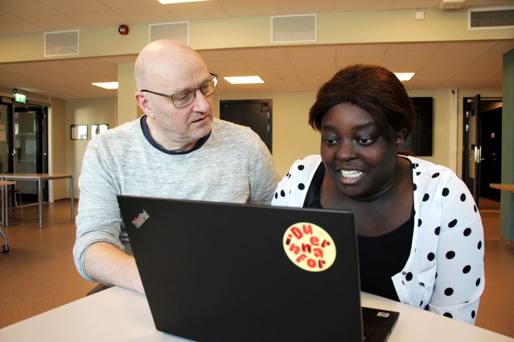 Vaksen elev og ein lærar sit ved ein pc. Foto. 