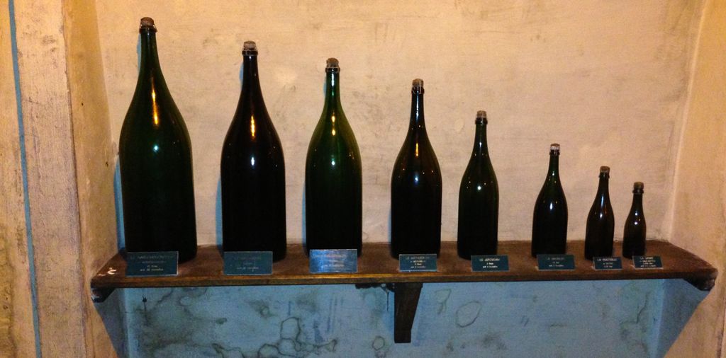 Flasker i ulik størrelse er stilt opp på ei hylle. Foto.