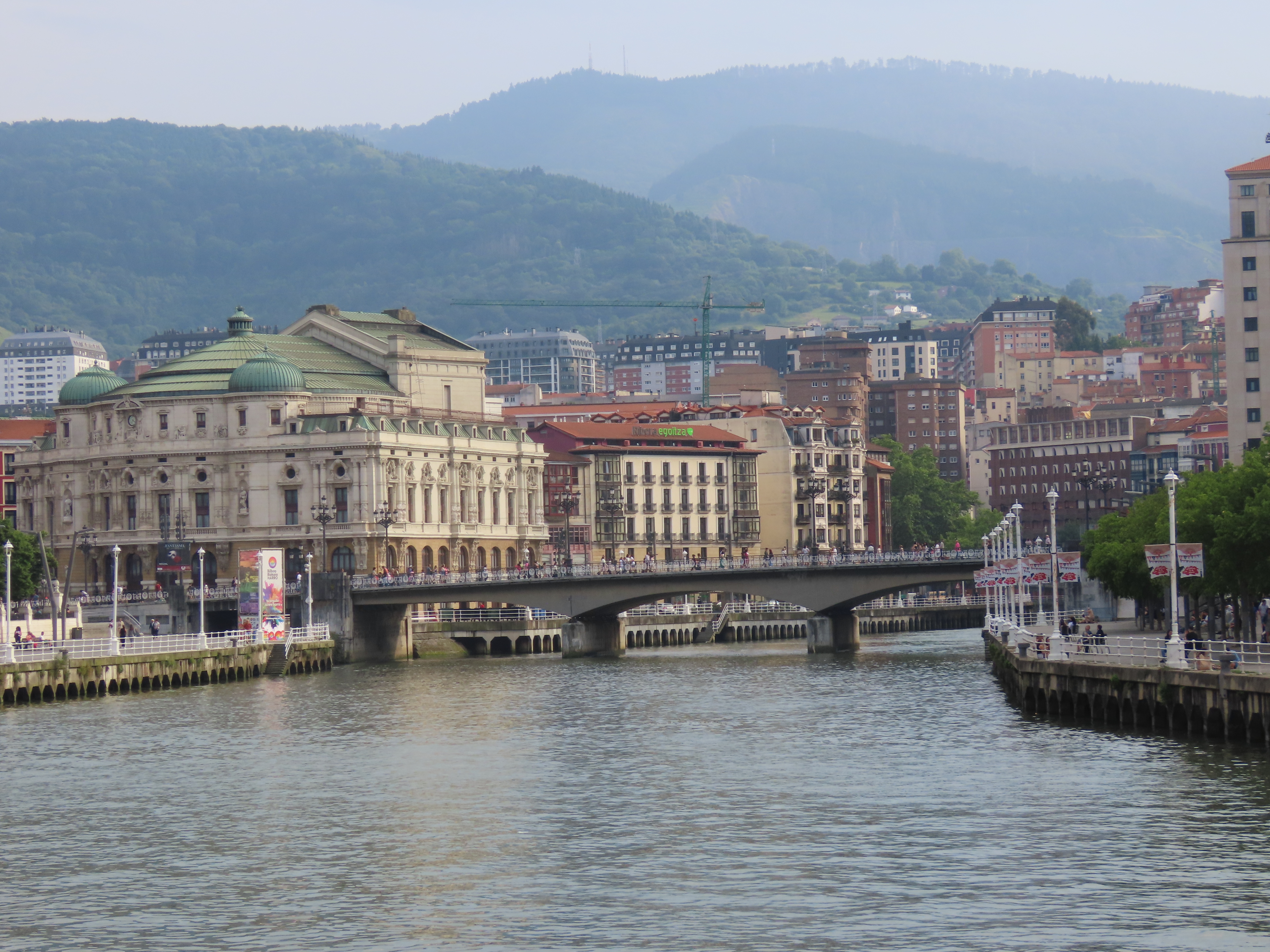 Ei elv med ei bru og flere store bygninger i bakgrunnen. Foto.