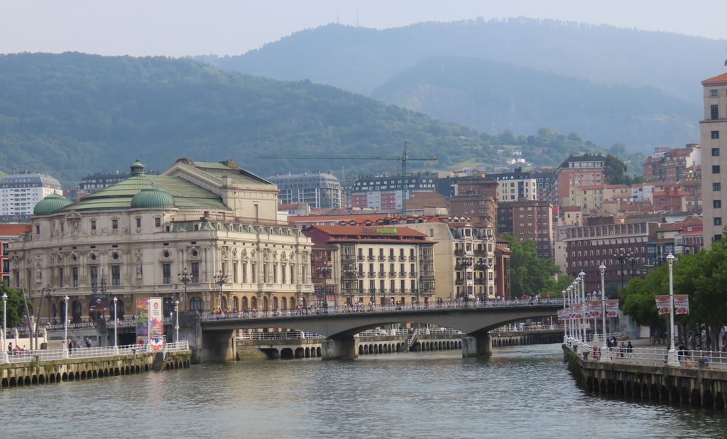 Ei elv med ei bru og flere store bygninger i bakgrunnen. Foto.