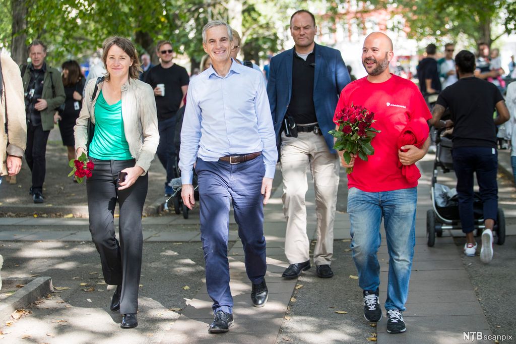 Smilende mennesker går nedover en gate. To av dem bærer buketter med røde roser. Foto. 