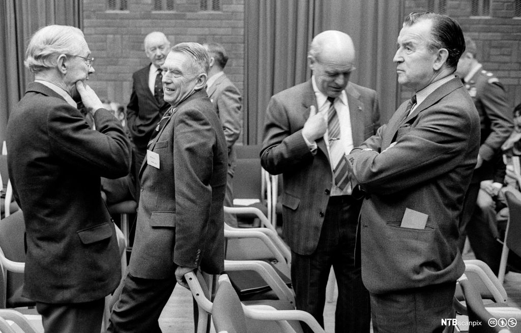 Dresskledde menn som snakker sammen og ler. De ser ut til å ha en pause i et offentlig program. Foto. 