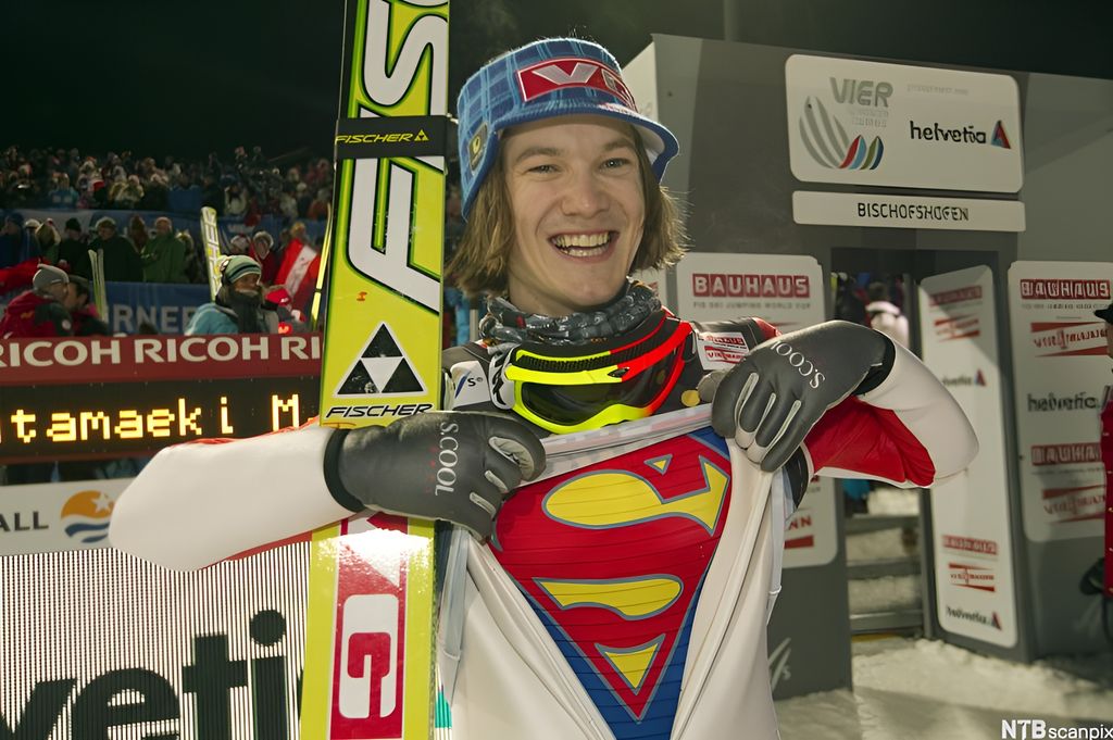 Ein strålande nøgd skihoppar viser at han har Supermann-trøye under hoppdressen. Foto.