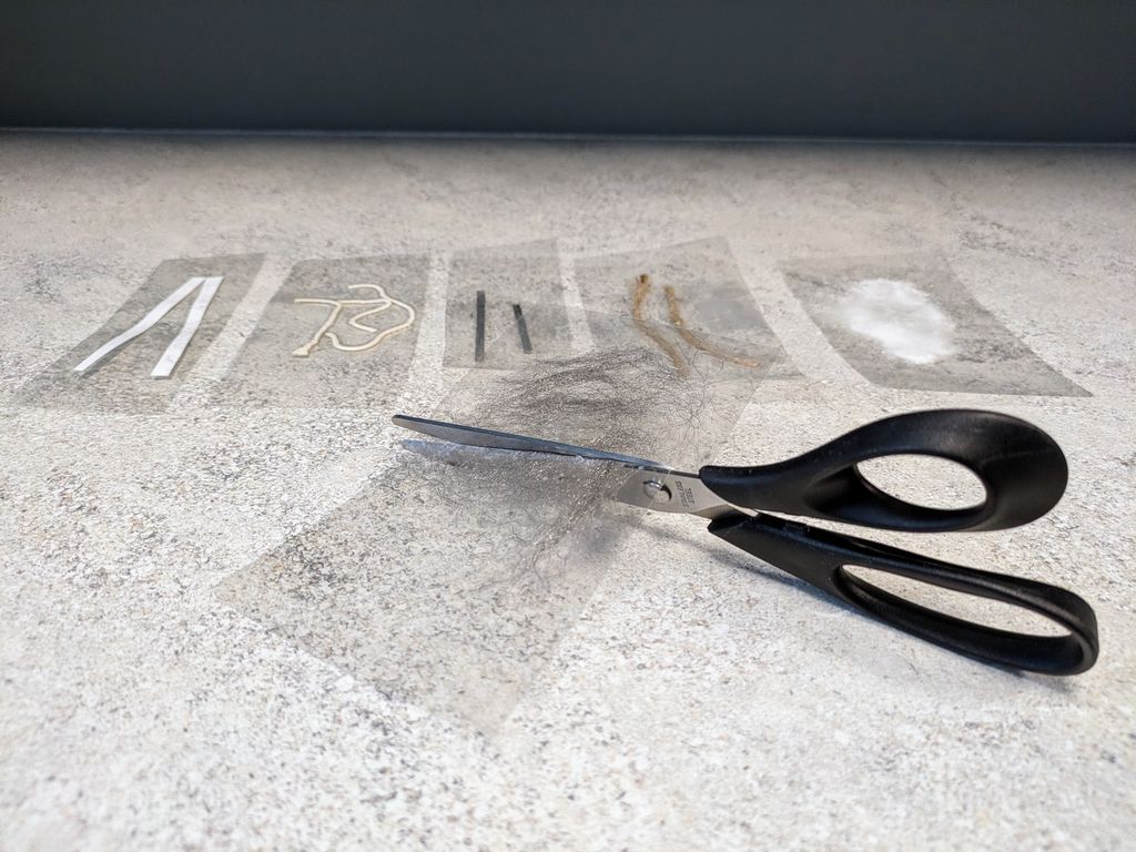 Ulike materialer er laminert med et plastark. Ei saks klipper gjennom lamineringsark med stålull. Foto.