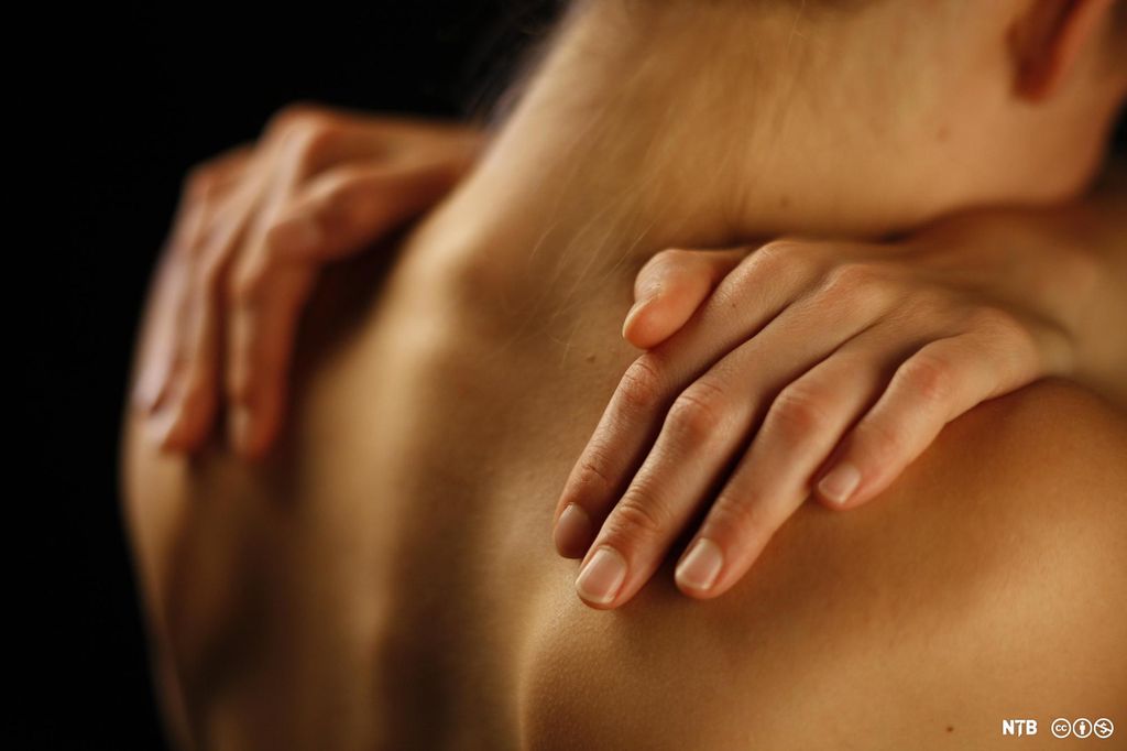 Hendene til en kvinne hviler på skuldrene til en mann. Foto.